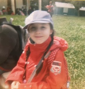 Photo de moi à 9 ans avec 2 tresse, une casquette rose et un K-Way rouge